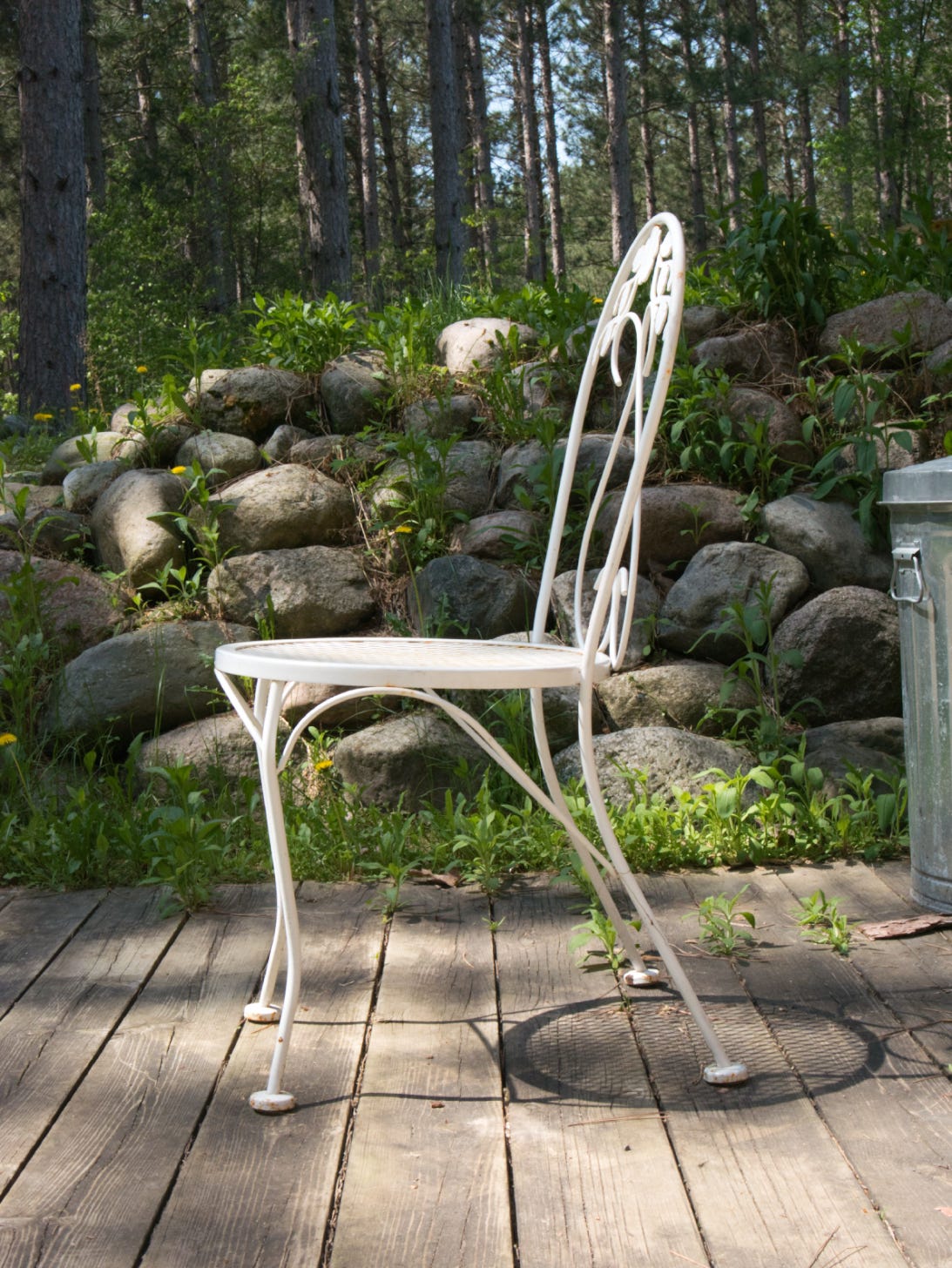 White chair foreground. Large rocks and trees in background.