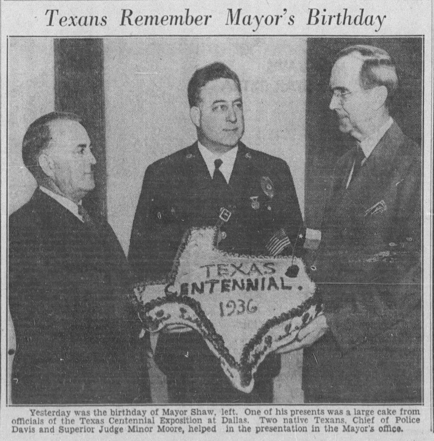 A newspaper clipping of three men standing around a white cake shaped like the state of Texas. It has white frosting with dark lettering and trim. The lettering reads "Texas Centennial. 1936."