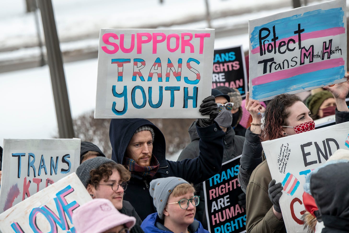 Protestors standing together holding signs urging our politicians to protect trans youth.