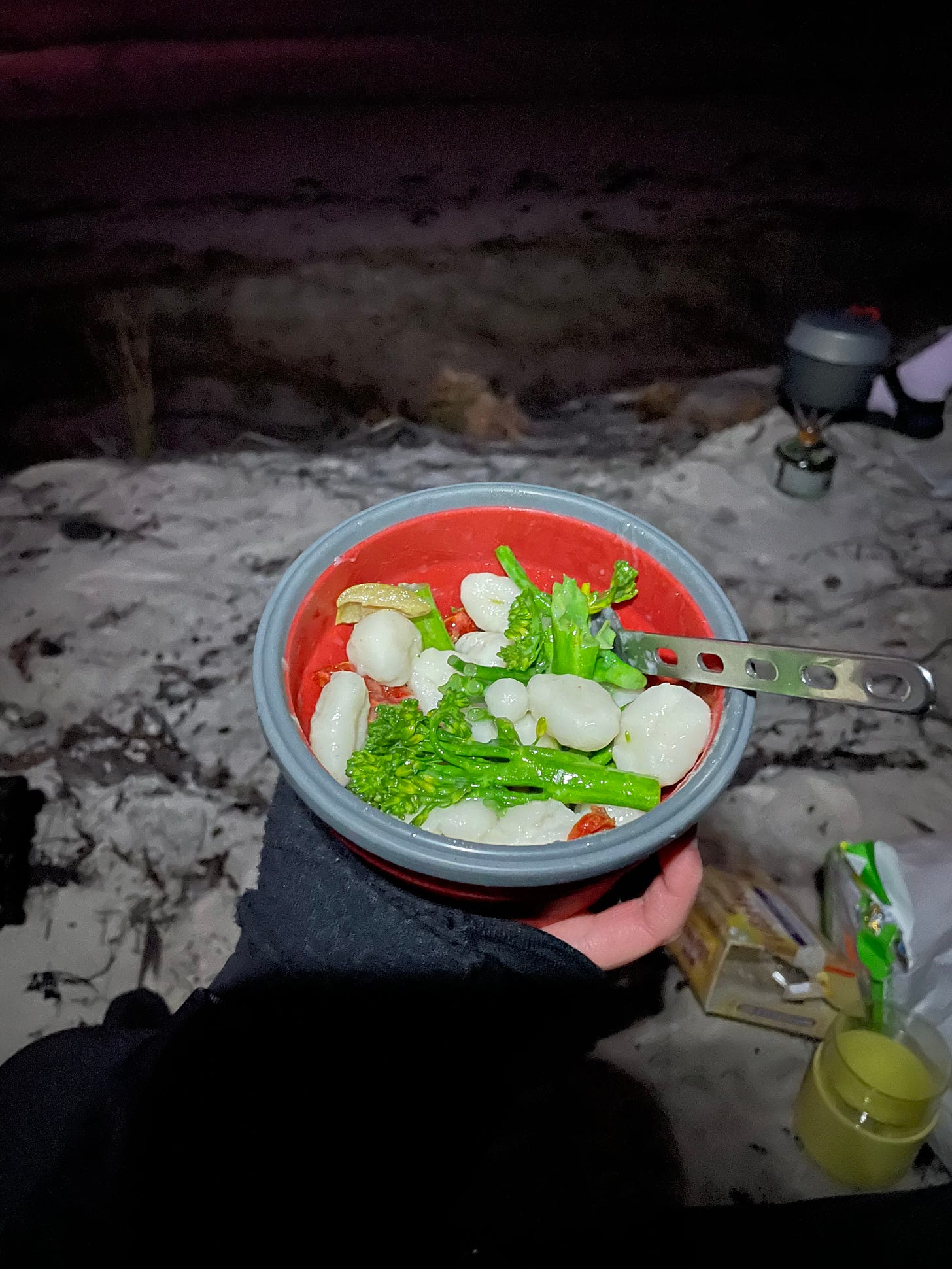 Gnocchi and broccolini in a collapsible bowl at a campsite at night.