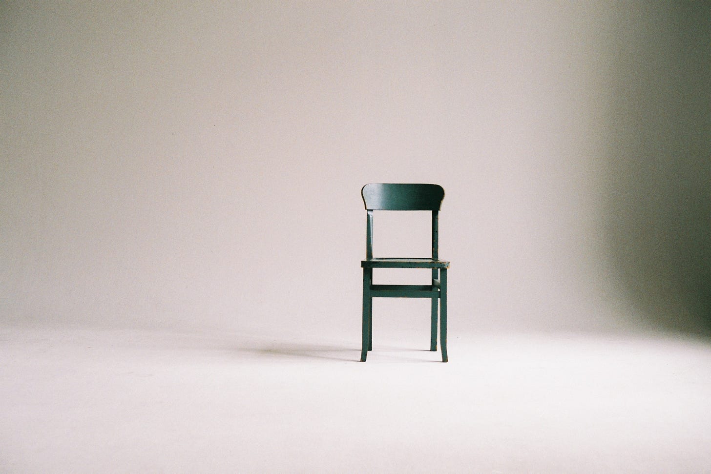 A wooden chair painted green is sitting in a room on a white drape, as if it’s being photographed for a fashion or architecture magazine spread.