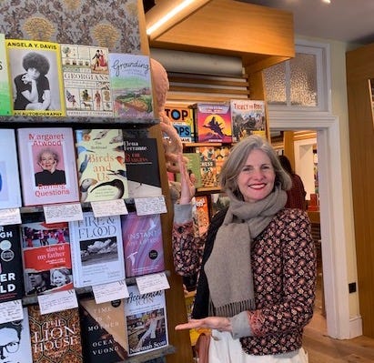 Lulah standing in front of a bookshelf containing her book, Grounding, amongst others