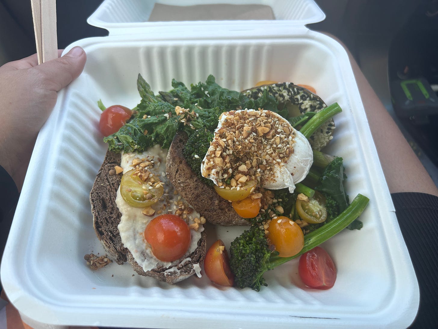 A takeaway container full of vegetables, with a poached egg and sourdough toast.