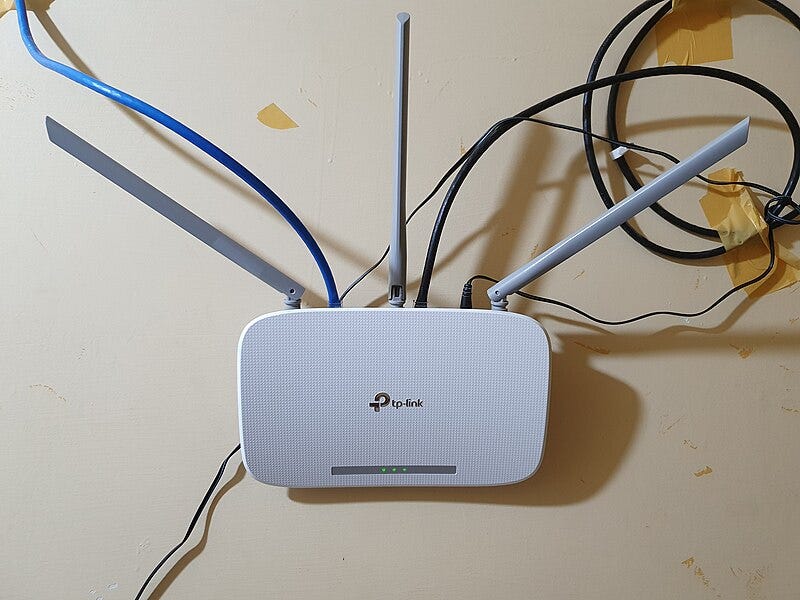 A white Wi-Fi router with antennae and cables coming from it, labeled "tp-link"