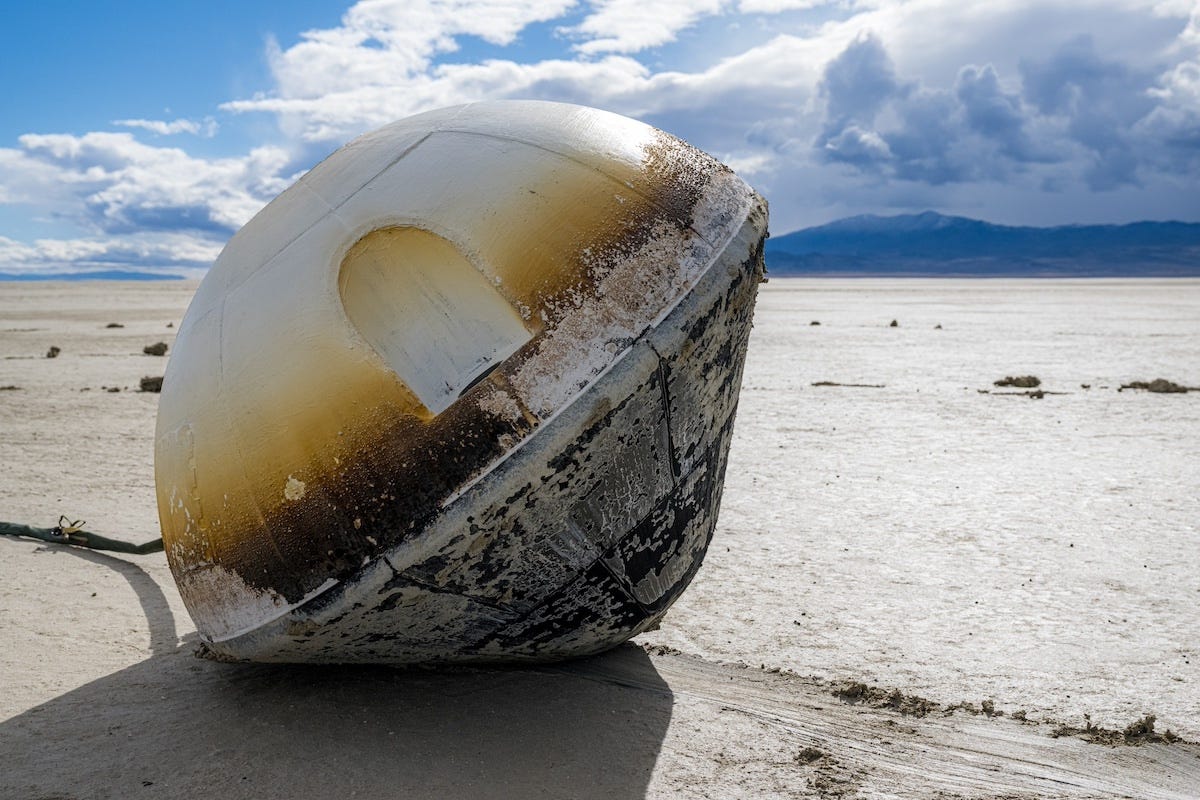 A weathered ceramic heat shield rests on a flat, desolate landscape under a cloudy sky.