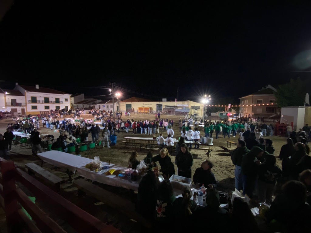 Lots of people eating outside in a square with table and chairs at night