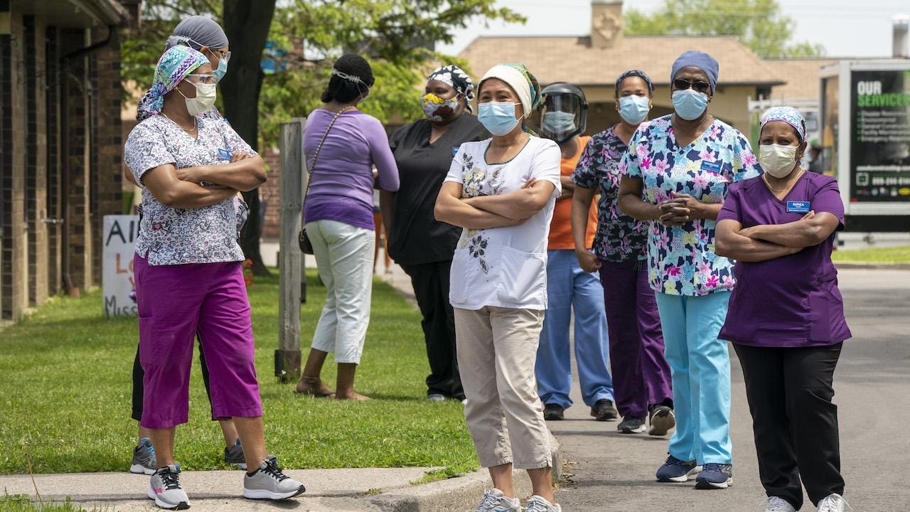 a group of workers wearing scrubs and masks stand outside an LTC home