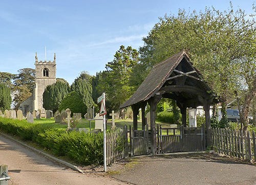 A wooden lychgate with a pointed roof at the entrance to a churchyard. A wooden lychgate with a pointed roof at the entrance to a churchyard.