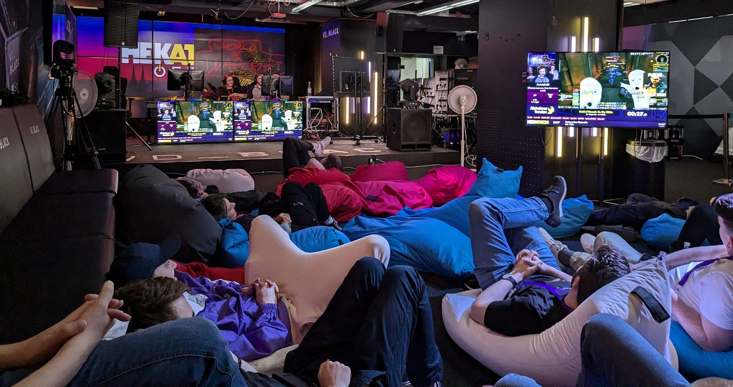 View across the crowd area full of bean bags towards the stage where people are speedrunning a World of Warcraft dungeon