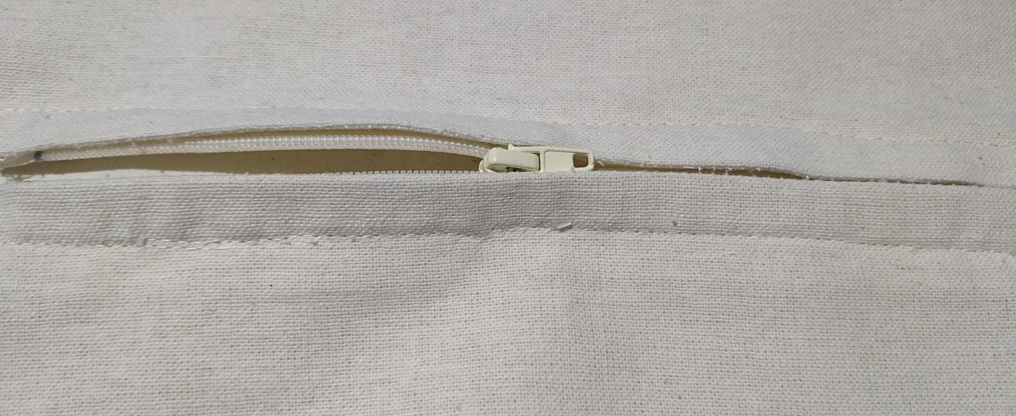 A half open zipper attached to a seam of beige fabric
