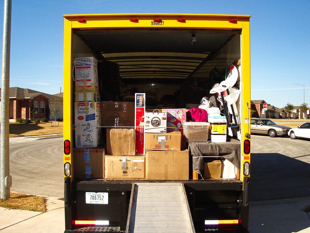 Yellow moving truck half full of boxes, parked on a cul-de-sac under a blue sky. "Moving truck" by TheMuuj is licensed under CC BY-SA 2.0.