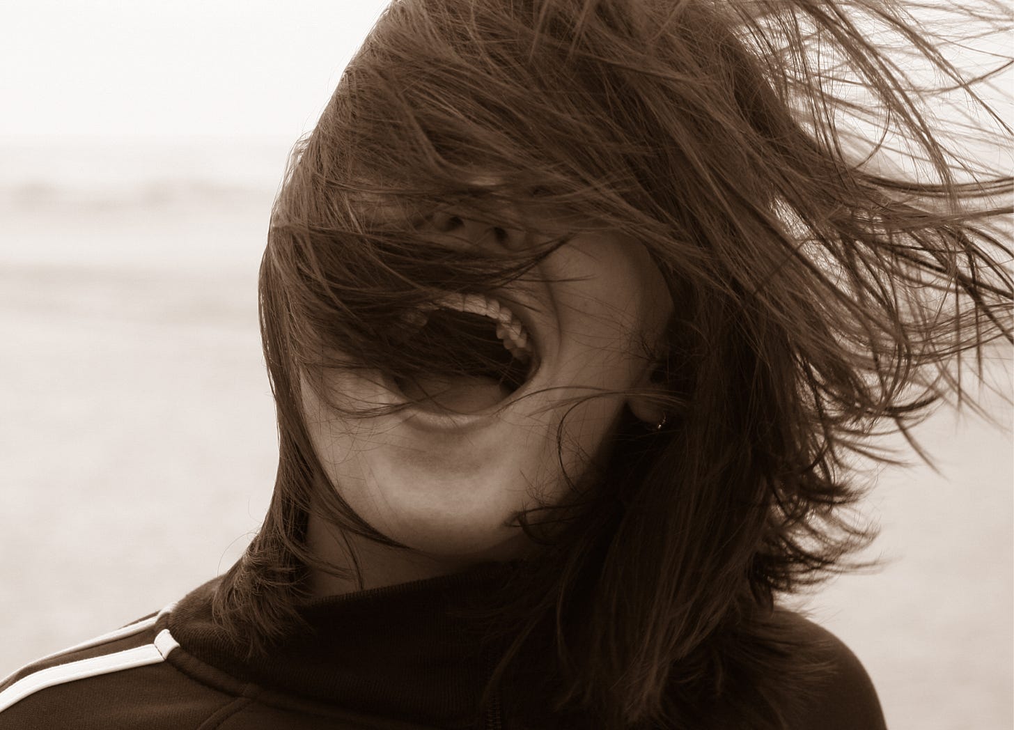 Woman laughing as her hair blows back. Photo courtesy of roundhill via Canva.