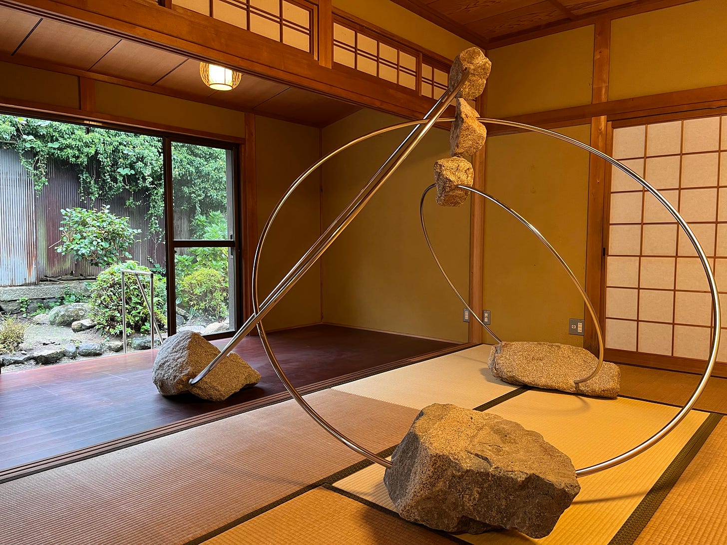 a sculpture comprising rocks on big metal rings touching inside a tatami room