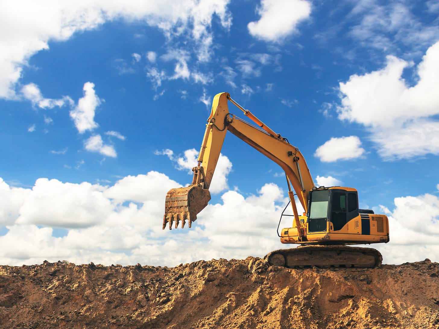 photo of an excavator on a pile of dirt against a blue sky with clouds