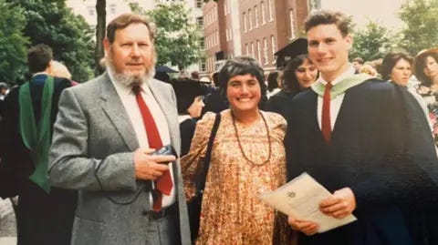 Keir Starmer/Tom Baldwin A smiling Keir Starmer wears a graduation gown and holds a certificate. His parents stand beside him.
