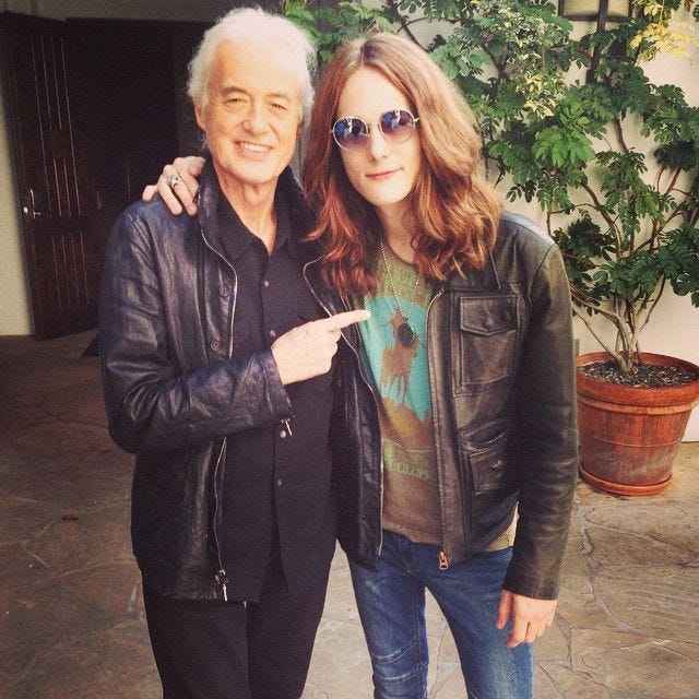 This may contain: an older man standing next to a young woman in front of a potted plant