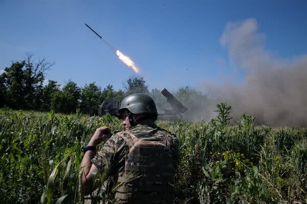 A soldier standing in a field as a missile is fired in the background. 