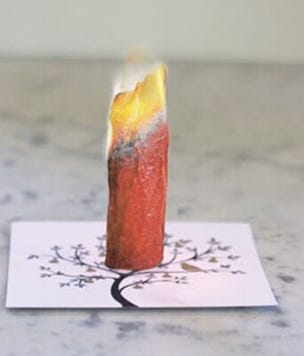 A piece of rolled up red paper stands rolled into a cylinder with the top set on fire