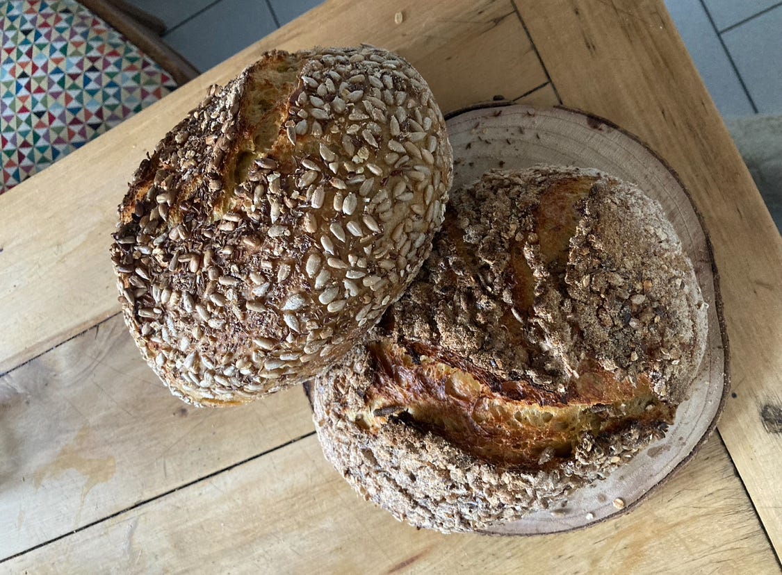 two loaves of seeded sourdough bread on a table.