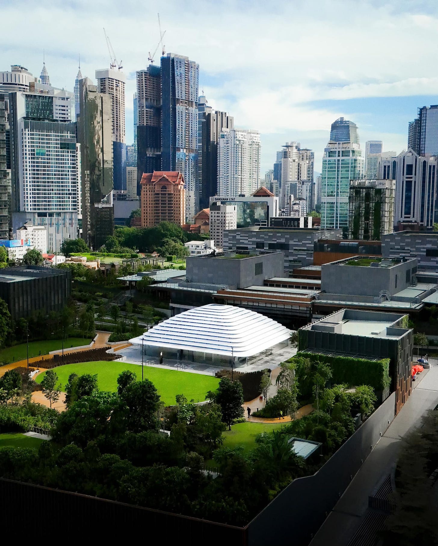 An aerial view of Apple The Exchange TRX and TRX City Park. In the distance, the skyscrapers of Kuala Lumpur rise.