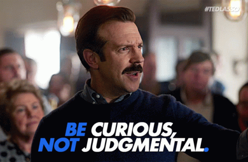 gif of Ted Lasso holding a dart with the words "be curious, not judgmental"