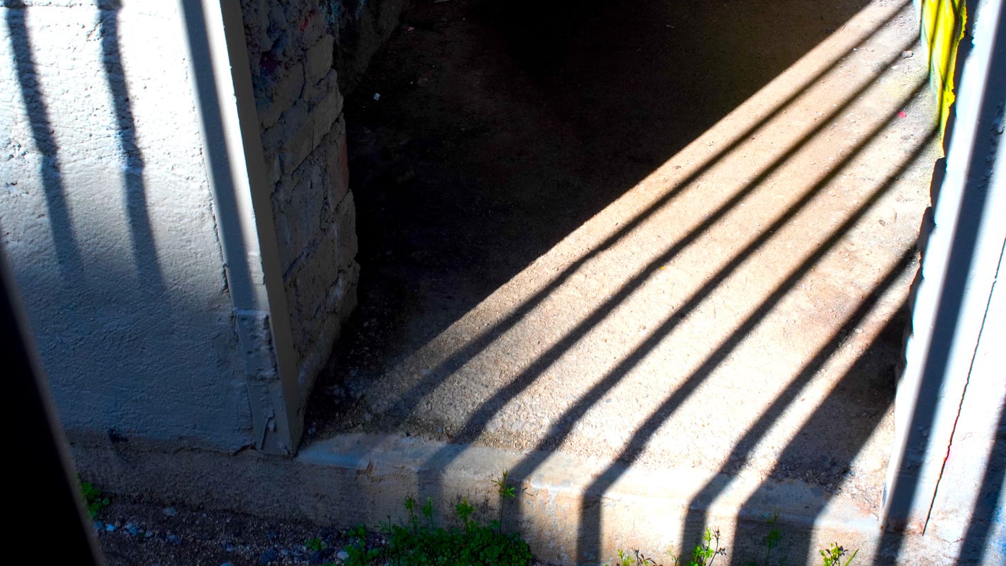 The shadow of bars on a cement floor in the late afternoon sun.