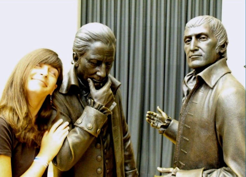 Young woman posed with two life-sized bronze statues of men from the colonial era