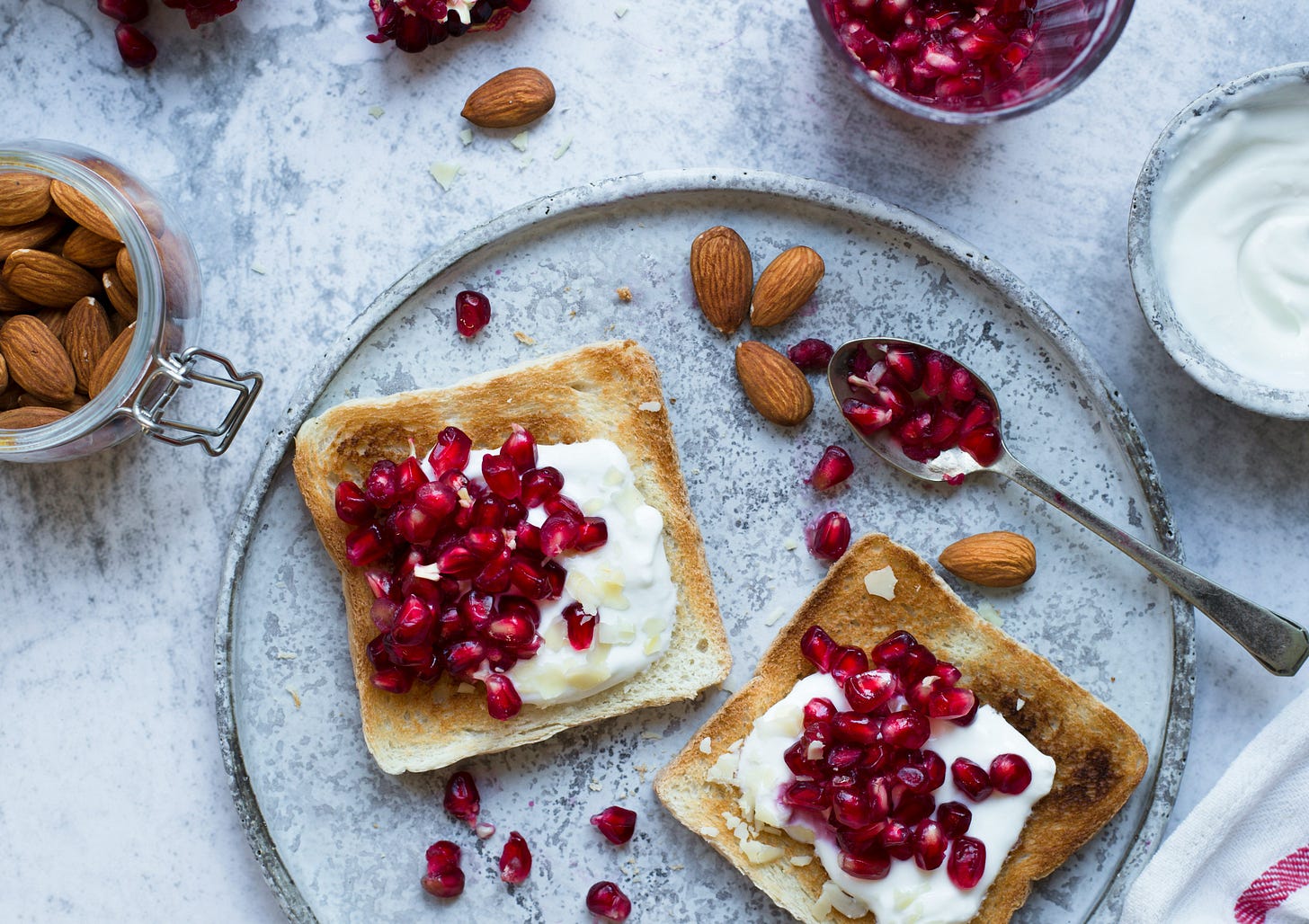 gray and white marble table with two pieces of toast topped with white ricotta cheese and red poemgranate seeds