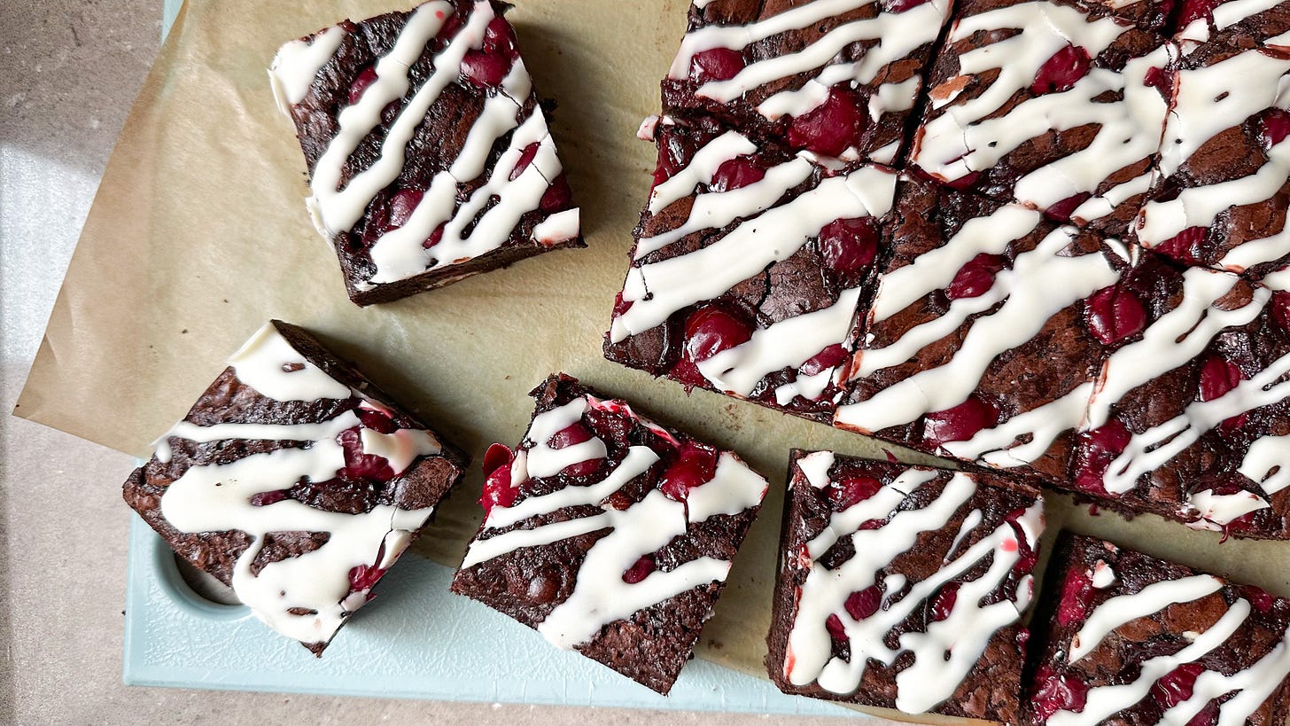 A photo of black forest brownies with big cherries inside and drizzled with white chocolate.