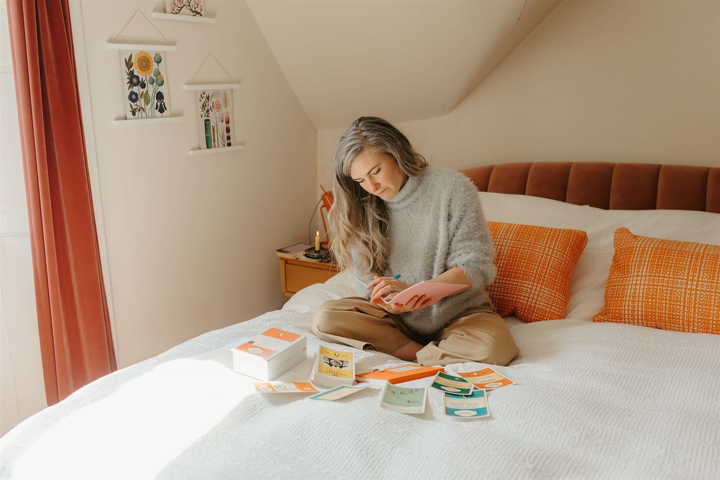 A white woman with grey hair sits on a bed, writing