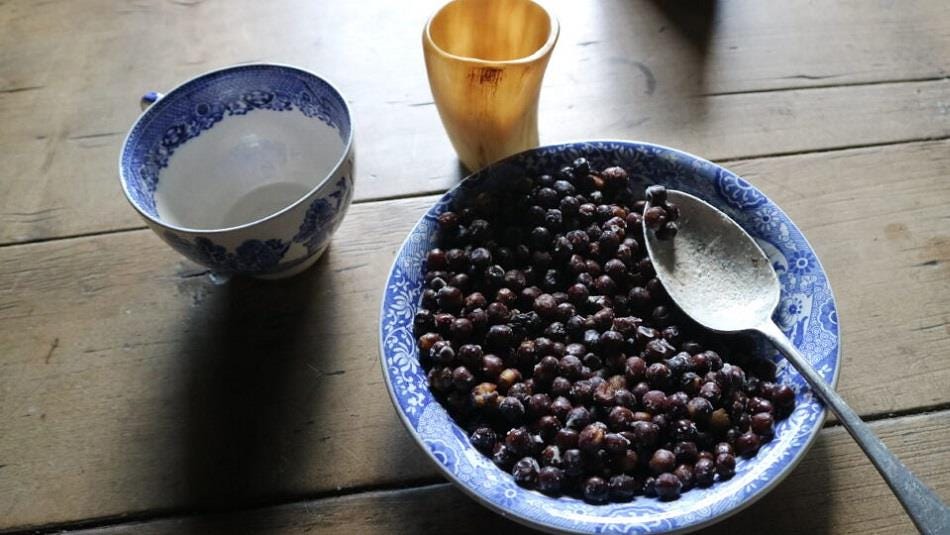 A blue china bowl, cup and horn glass on a wooden table.  The bowl holds Carlin peas, very dark and round