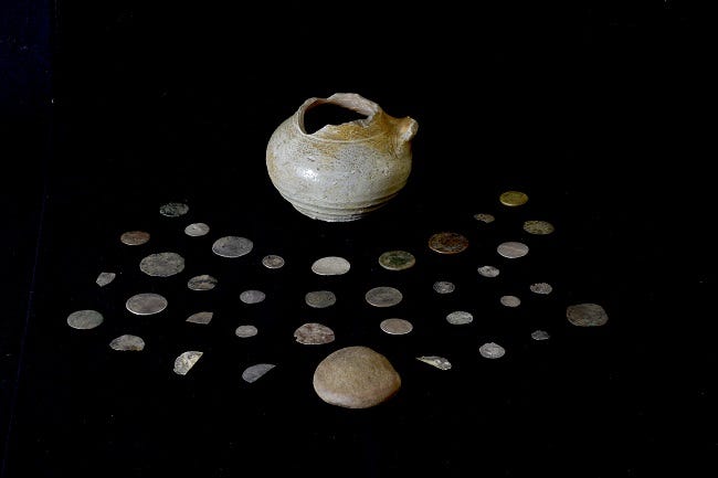 A group of 17th currency coins and a ceramic pot on a black background.