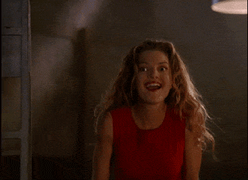 Glory from Buffy the Vampire Slayer smiling while doing an exaggerated sneaking motion and then putting a finger up to her lips.