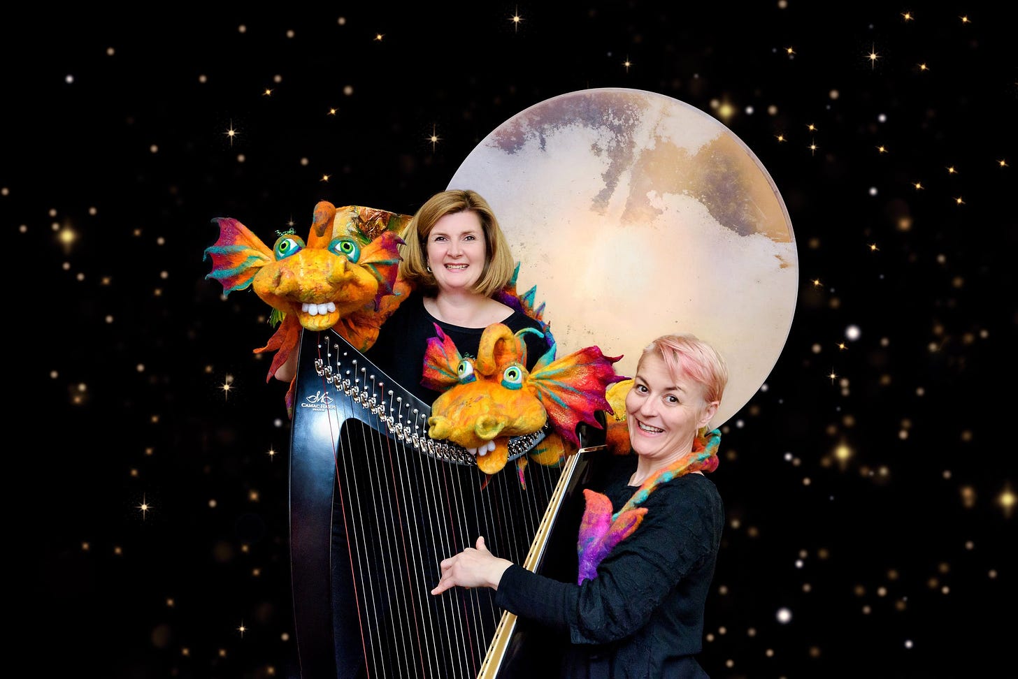 Two puppeteers with a harp and dragon puppets in front of a large moon and starry backdrop