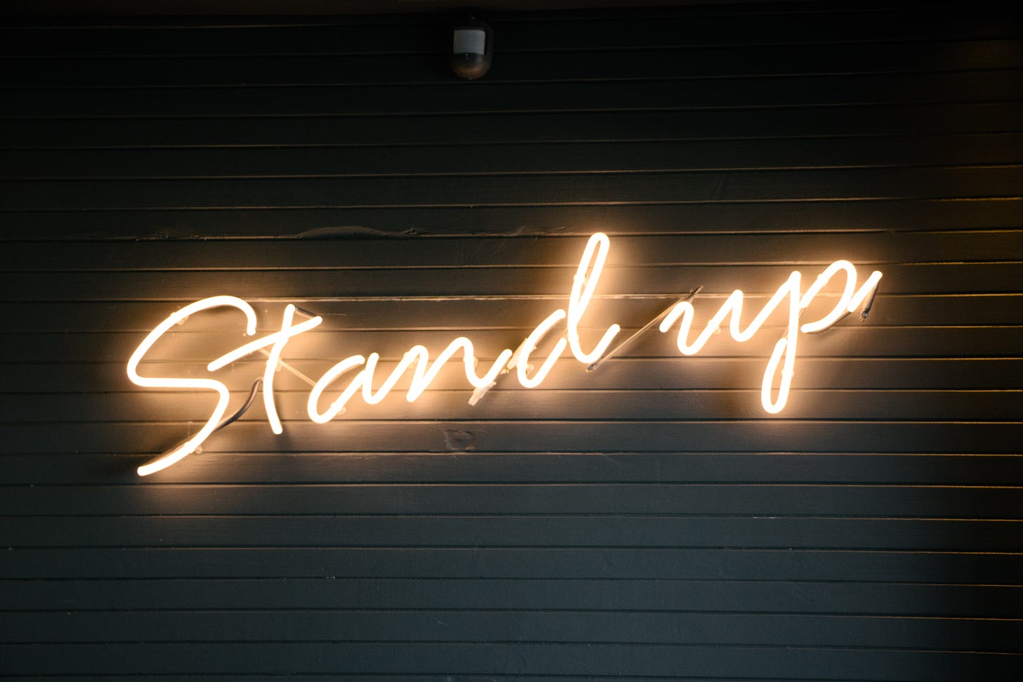 The phrase "Stand up" in a lighted sign on a slatted wooden backdrop