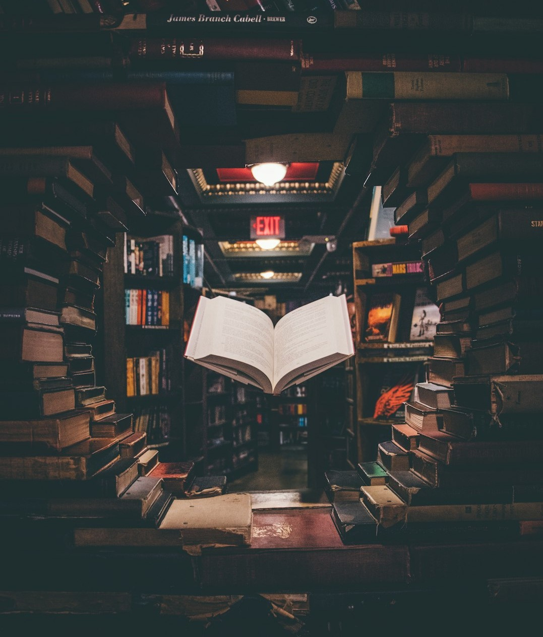 view of floating open book from stacked books in library view of floating open book from stacked books in library
