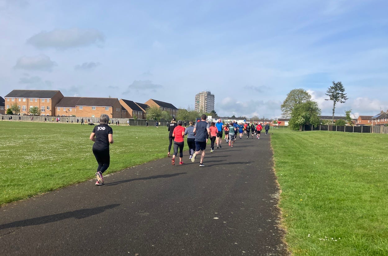 Runners on a pathway during the first lap of a parkrun event, with houses in the background and a clear sky above.