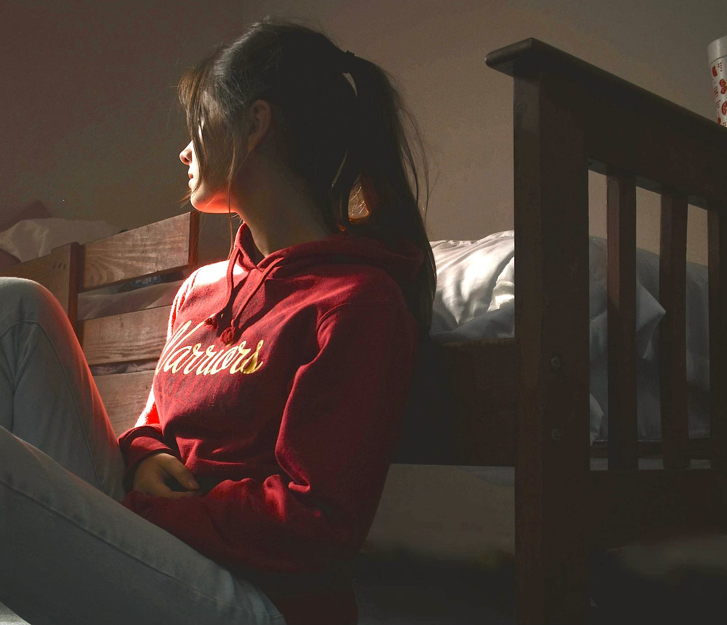 Woman in despair red sweatshirt leaning against bed