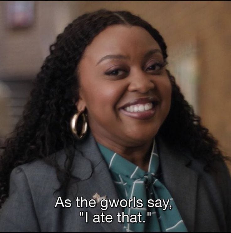 This may contain: a woman with curly hair wearing a gray suit and green shirt smiles at the camera