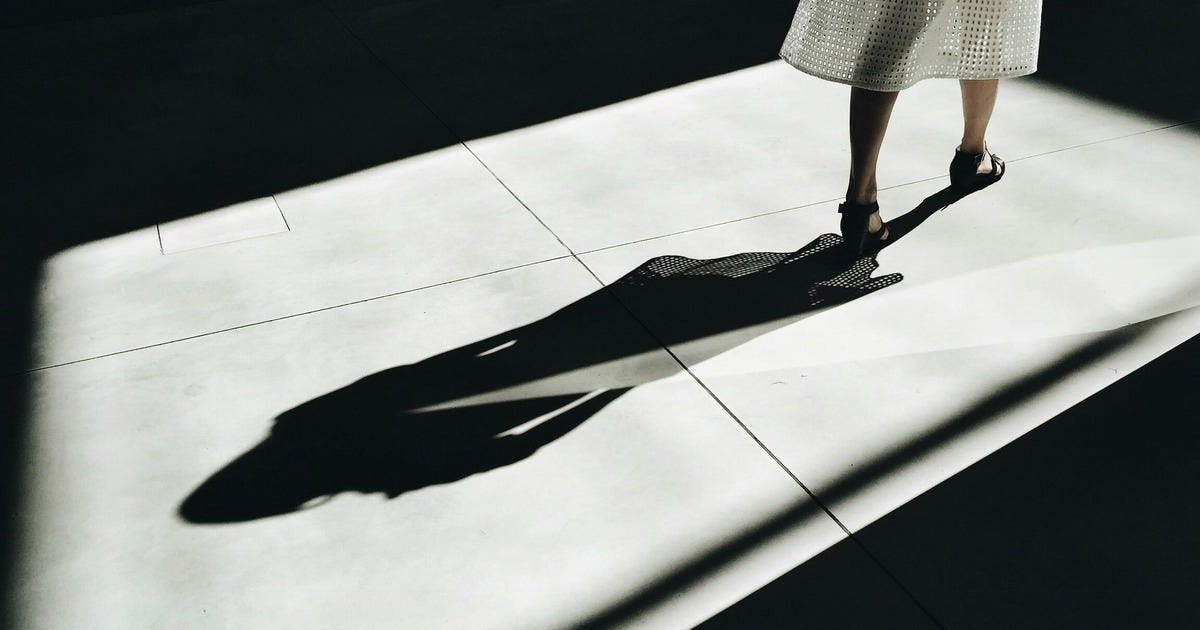 From Unsplash. A woman in heels walks in a patch of light, with a dark shadow cast behind her.