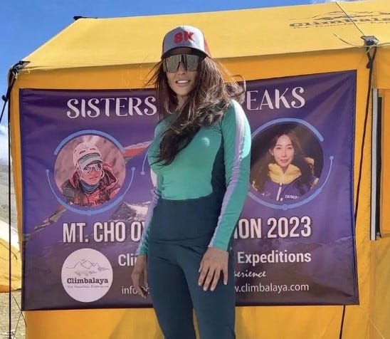 The climber stands on front of a tent with a banner featuring her climb and grace Tseng's.