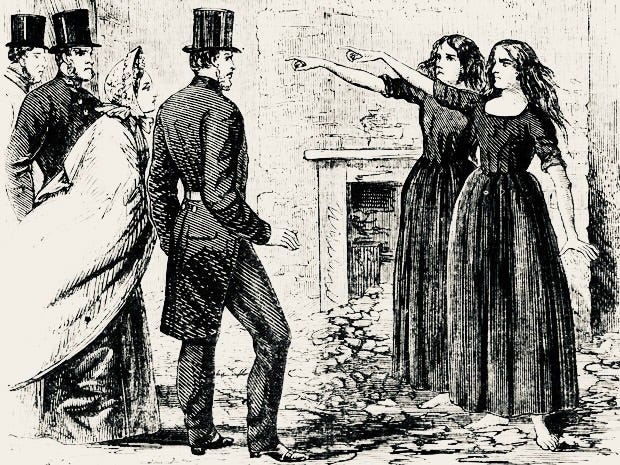 A newspaper illustration showing two women in black clothing, with dark flowing hair. They both raise their right arm to point into the distance. Behind them is a fireplace, and the floor appears dirty. They have bare feet. On the left of the image are three smartly-dressed men with top hats and one woman in a long cape and bonnet.