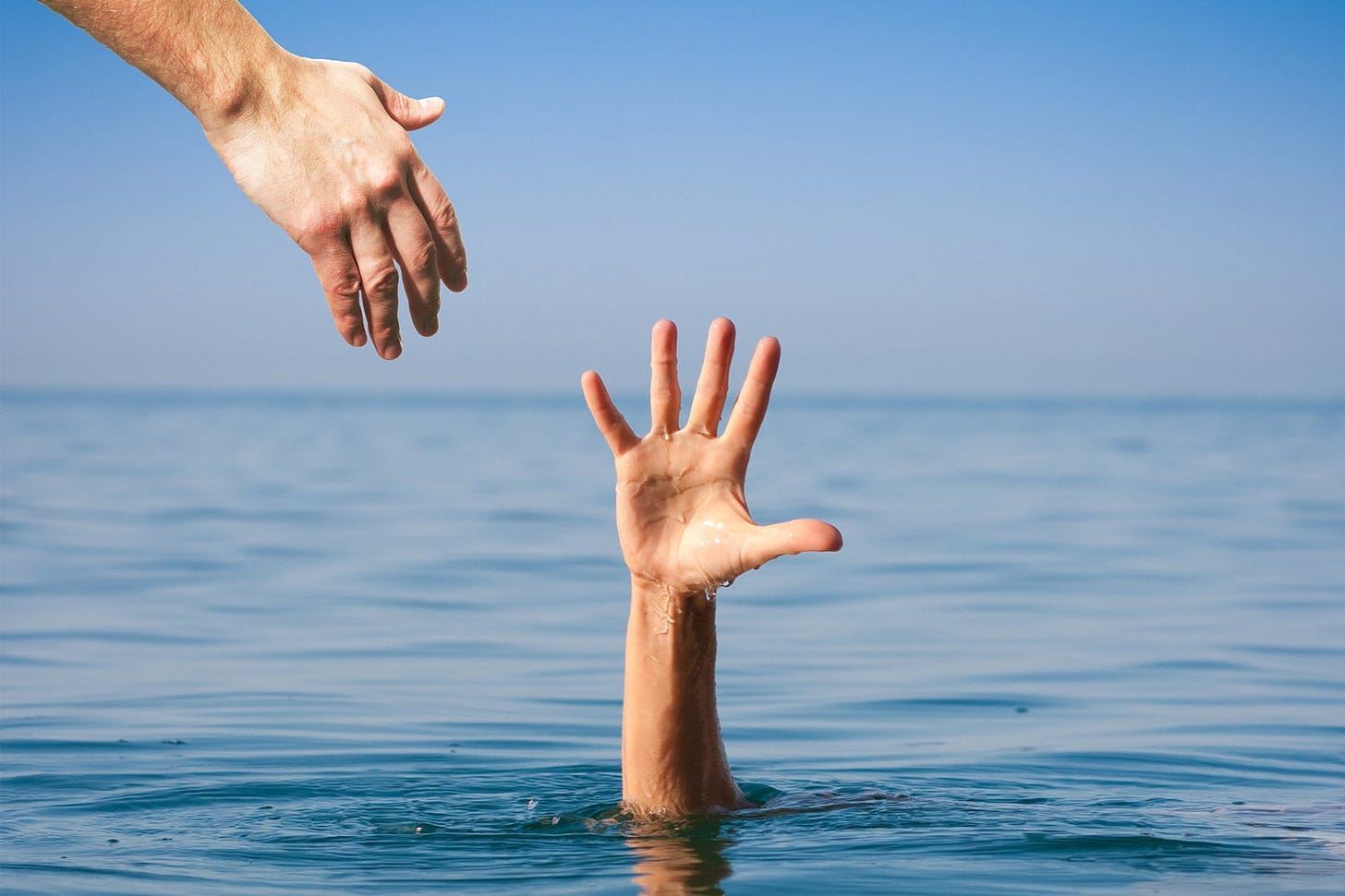 Hand of a drowning person reaching out of the water. Another hand from above offers help.