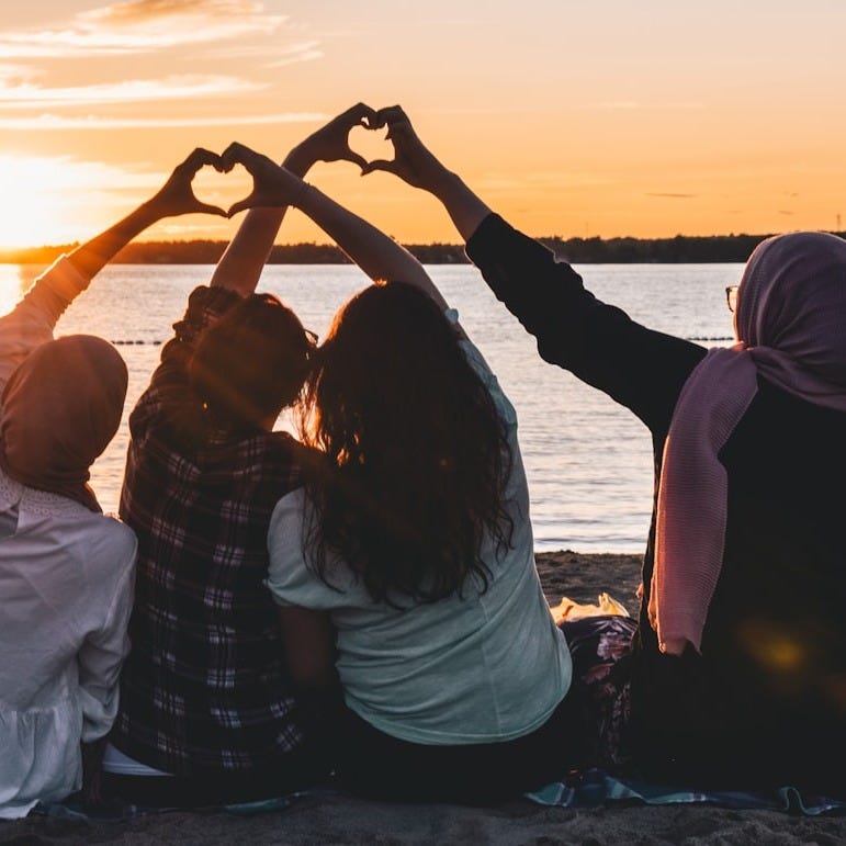 four people sitting on shore forming hearts with their hands during golden hour four people sitting on shore forming hearts with their hands during golden hour
