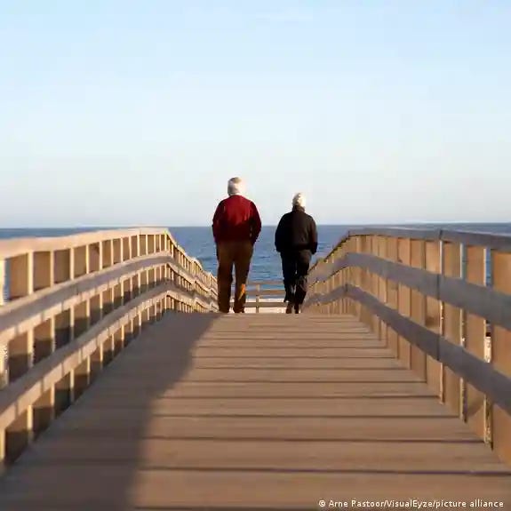 An elderly couple seen from behind walks on a wooden pier