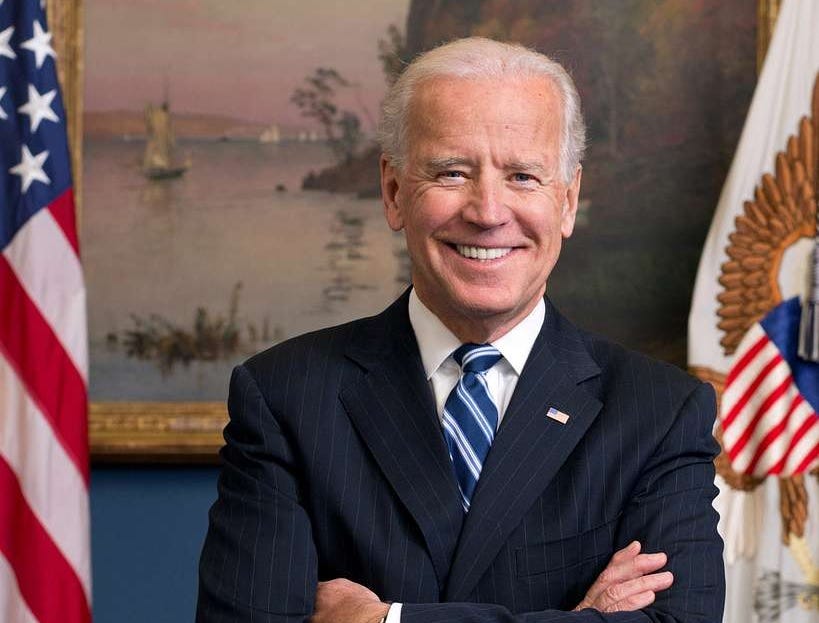 photo of Joe Biden, smiling, his arms crossed, in the White House