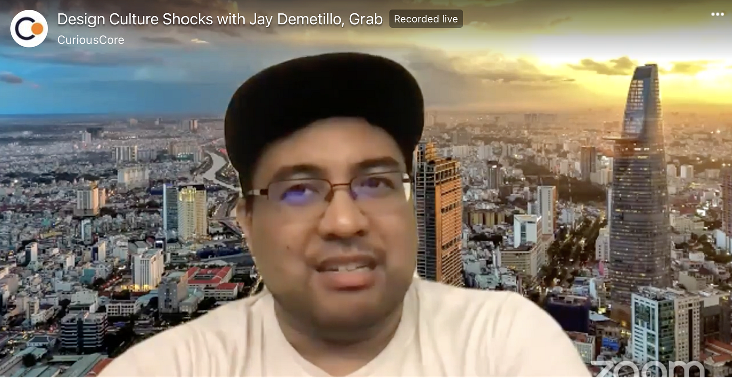 Screenshot of Jay Demetillo in a black cap and white t-shirt speaking in front of a cityscape Zoom background.