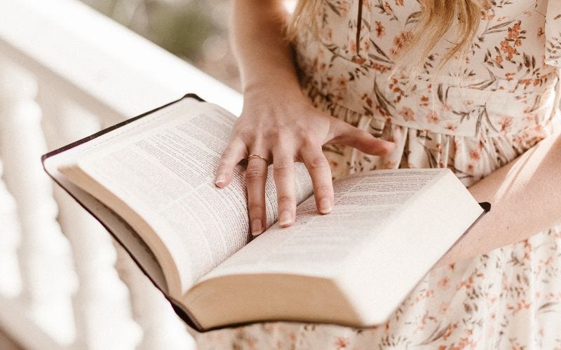 Closeup of a woman holding a Bible, leaning against a front porch railing.