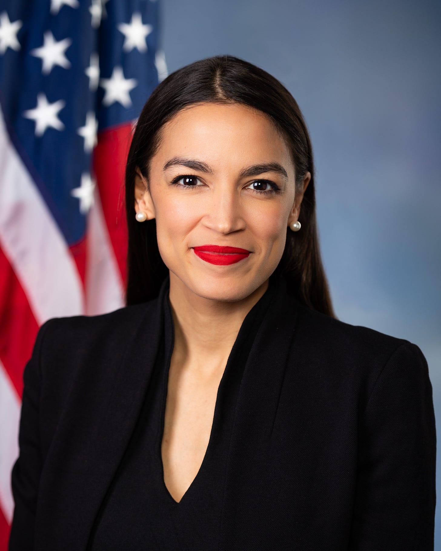 AOC official portrait; wearing a black blouse; american flag behind her.