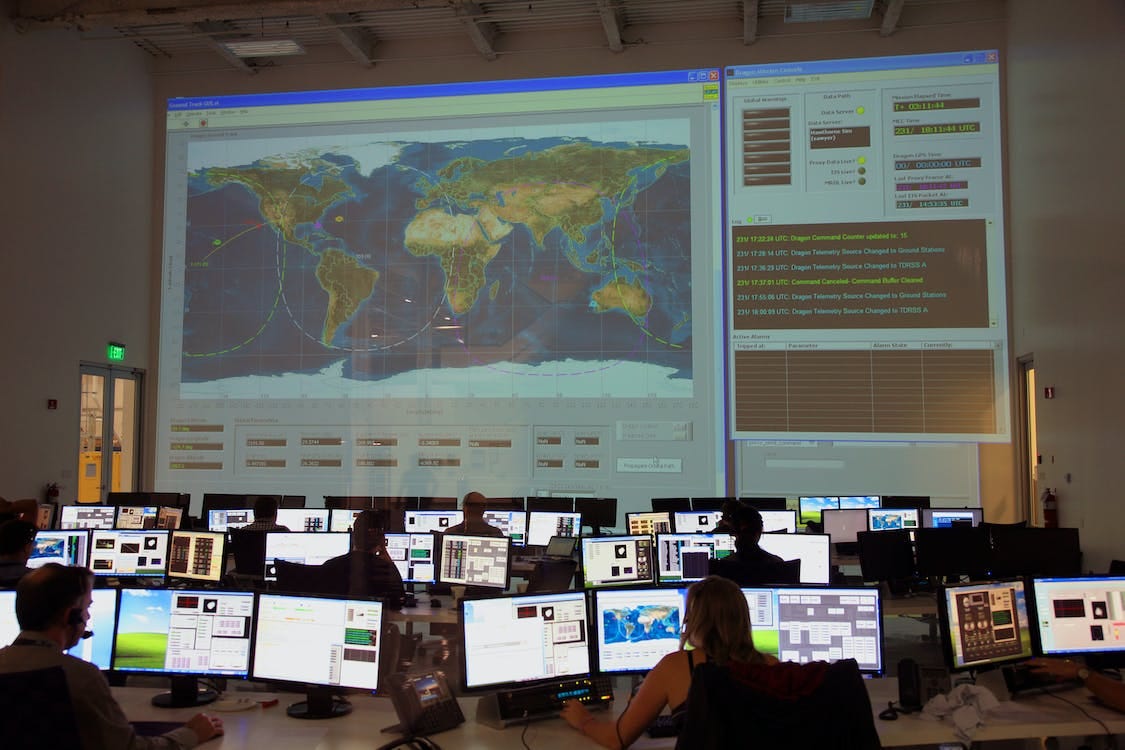 Free Back view of unrecognizable employees working on computers in flight control room with big interactive map on wall and analyzing data Stock Photo
